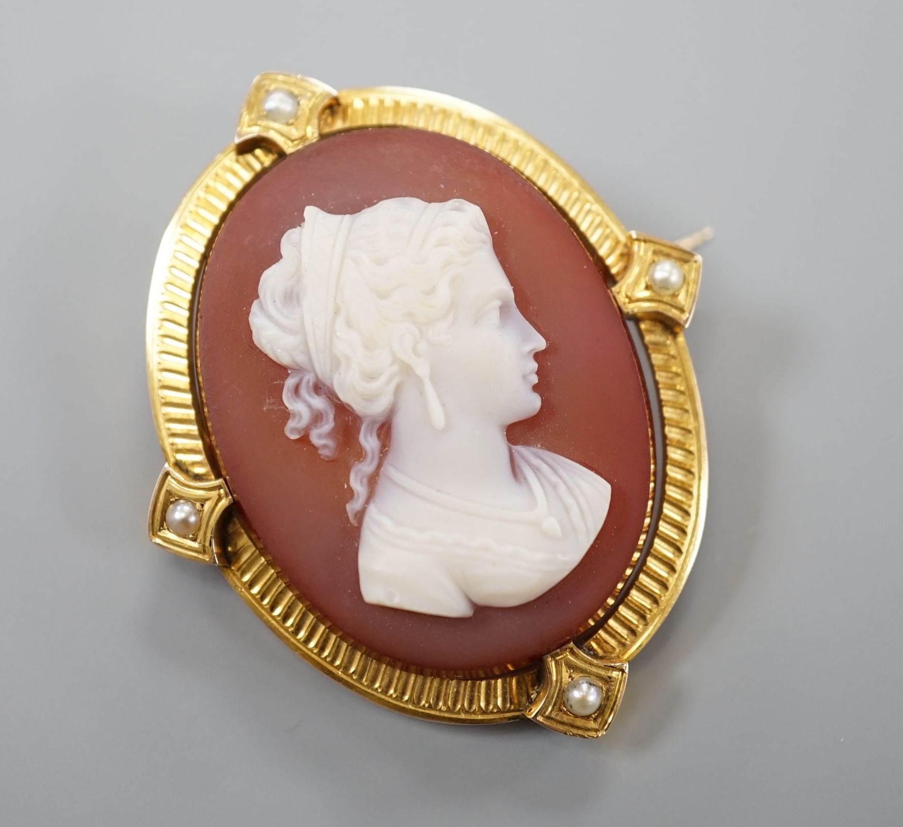 A late Victorian yellow metal and split pearl mounted oval sardonyx camel set brooch, carved with the bust of a lady to sinister, 47mm, gross 12.3 grams.